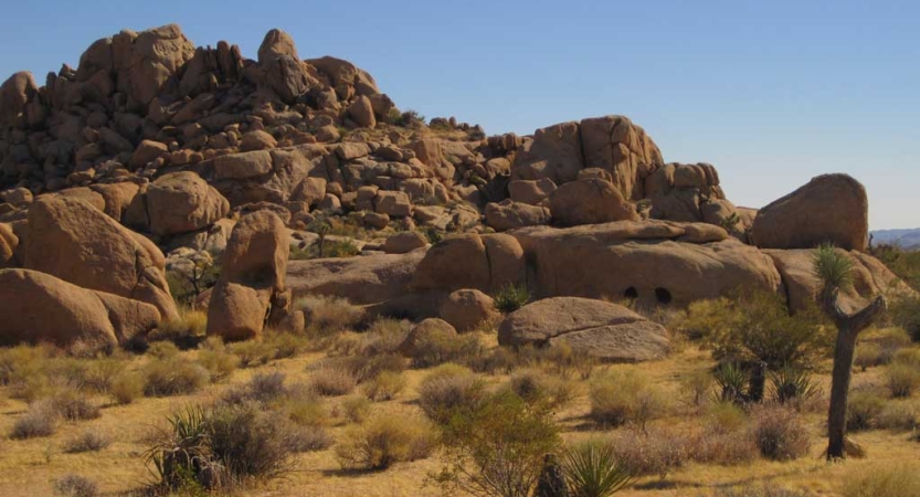 Large boulders make up a rock formation in a desert landscape under blue skies. 